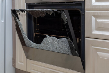 Opened broken oven door in the kitchen, side view, close-up. Broken glass from overheating. Broken...