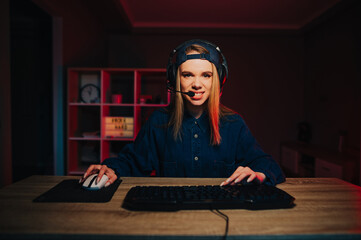 Concentrated gaming lady playing computer games at home in a cozy room with red light, looking into the camera clenching her teeth.
