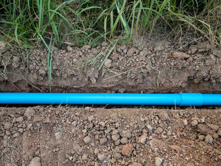 The small PVC pipe is laying in the trench near the pavement for the water supply system.