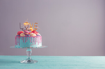 cake with pink and blue decor and burning sparkler with text love