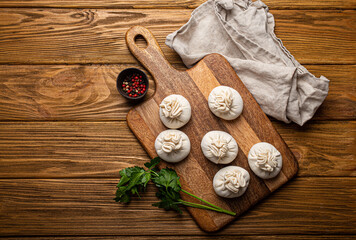 Raw freshly made Khinkali, traditional dish of Georgian Caucasian cuisine, dumplings filled with ground meat on white plate with herbs on wooden rustic background table top view space for text
