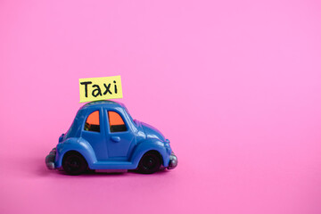 A small blue retro car on a pink background with the inscription taxi. Transportation of children. Taxi for children. Taxi.