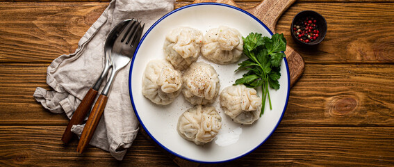 Khinkali, traditional dish of Georgian Caucasian cuisine, dumplings filled with ground meat on white plate with herbs on wooden rustic background table top view
