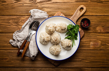 Khinkali, traditional dish of Georgian Caucasian cuisine, dumplings filled with ground meat on white plate with herbs on wooden rustic background table top view
