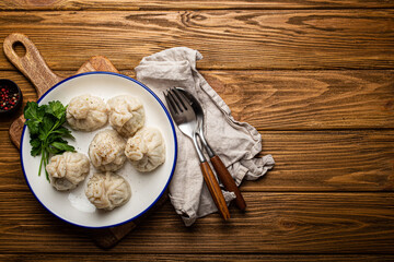 Khinkali, traditional dish of Georgian Caucasian cuisine, dumplings filled with ground meat on white plate with herbs on wooden rustic background table top view
