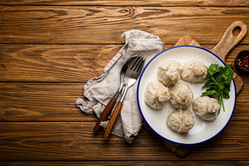 Khinkali, traditional dish of Georgian Caucasian cuisine, dumplings filled with ground meat on white plate with herbs on wooden rustic background table top view
