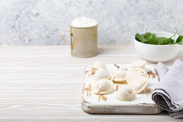 Fototapeta na wymiar Raw uncooked pelmeni, traditional dish of Russian cuisine, dumplings with minced meat filling on white wooden cutting board kitchen rustic background table food composition angle view space for text