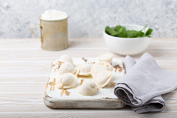 Raw uncooked pelmeni, traditional dish of Russian cuisine, dumplings with minced meat filling on white wooden cutting board kitchen rustic background table food composition angle view space for text