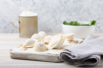 Obraz na płótnie Canvas Raw uncooked pelmeni, traditional dish of Russian cuisine, dumplings with minced meat filling on white wooden cutting board kitchen rustic background table food composition angle view space for text