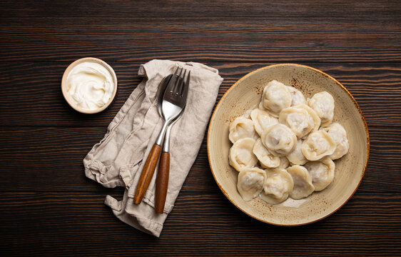 Pelmeni, traditional dish of Russian cuisine, boiled dumplings with minced meat filling on plate with sour cream sauce on wooden rustic background table from above food composition