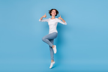 Fototapeta na wymiar Full size photo of attractive student age girl jumping showing thumbs-up promotion isolated on blue color background