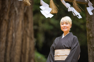 神社の境内に立つ着物姿（大島紬）の金髪日本人女性