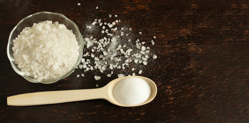 Glass vase with rock salt, wooden spoon with salt on a dark wooden background. ingredient