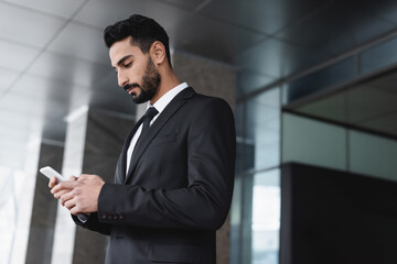 bi-racial guard in suit messaging on mobile phone outdoors.