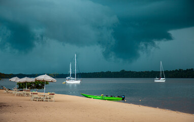 Yachts standing on the river on a clear sunny day against the background of green trees and dark storm clouds, Guyana. Travel adventure ships, subtropics. © Victor1153