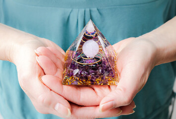 Close up view of woman hands holding and using Orgonite or Orgone pyramid at home while meditating....
