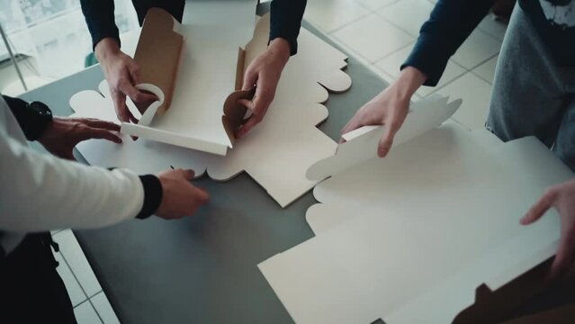 A group of three young people folds cardboard boxes for gifts for the holiday, DIY, handmade, craft