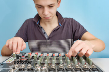 The boy sits at the mixing console and adjusts the sound with fenders.