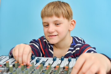 The boy sits at the mixing console and adjusts the sound with fenders.