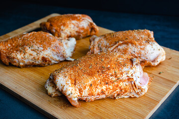 Bone-in Skin-on Raw Chicken Thighs Rubbed with Spice Mixture: Uncooked spice-rubbed chicken thighs on a wooden cutting board