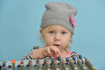 A little girl in a hat wants to make her own sound on the mixing console.