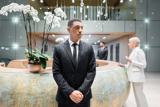 African American Security Man Looking Away Near Blurred Businesswoman At Hotel Reception.