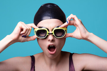 woman swimmer, in a swimming cap, glasses and a swimsuit, blue background