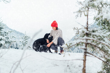 Fototapeta na wymiar A young woman in warm knitted clothes walking her 2 dogs in a picturesque snowy mountain outdoor. Female smiling and playing with pets. Human and pets winter concept image