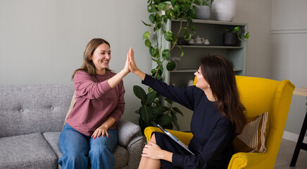 a happy female psychologist is sitting in a chair celebrating a solved problem with a patient. Successful psychotherapy