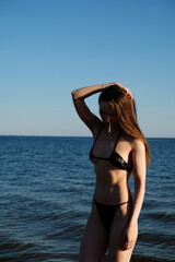 Girl in a black bikini with a cigarette in her mouth stands in the sea. Summer fashion photo