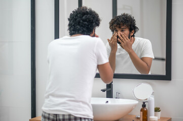Concentrated young man examining his facial skin