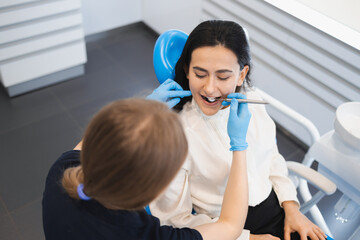 Image of pretty young woman sitting in dental chair at medical center while professional doctor checks her teeth