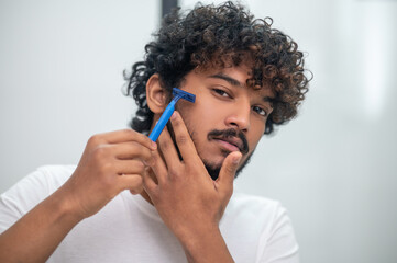 Young man shaving his face before the mirror