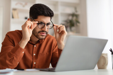 Confused Arab guy using laptop looking at screen