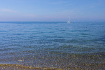 Panoramic view to Adriatic sea with pebble beach and white sailboat on horizon under blue sky on sunny day