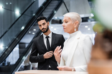 young bi-racial security man looking at camera near blurred business lady waiting at hotel reception.