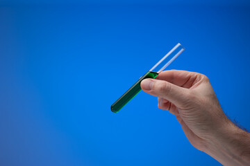 Medical test tube containing a green liquid held in hand by Caucasian male. Close up studio shot,...