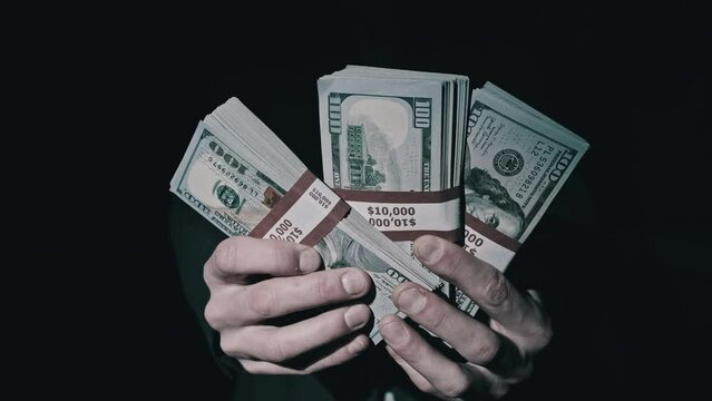 Three stacks of 10000 American dollars banknotes in bundles in male hands on black background. Man show pack of new 100 US dollar bills to the camera. Successful young freelancer holding pile of money
