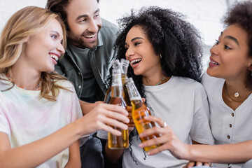 happy man and joyful interracial women clinking bottles of beer.