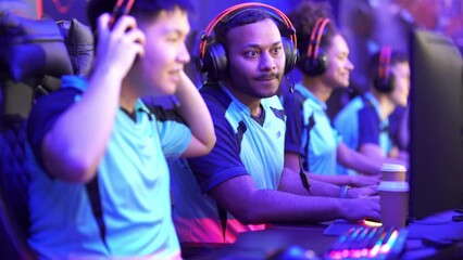 Group of multiethnic cybersport players in headsets sitting in front of computers and playing video games online indoors