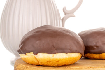 Two flavored chocolate doughnuts on a wooden tray with a ceramic milk jug, macro, isolated on a white background.
