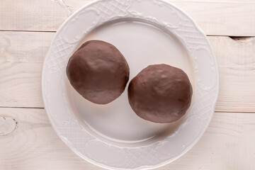Two sweet chocolate donuts on a white dish on a wooden table, macro, top view.