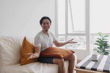 Happy Asian man sits and relax on the sofa in the living room of the apartment.