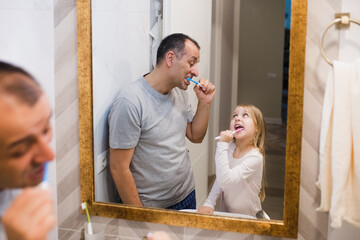 Father and daughter are brushing their teeth. 