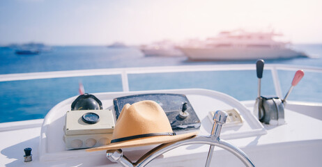 Travel hat lies on steering wheel of modern luxury yacht with sun light, concept banner trip on sea, boat rental.