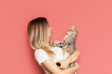 A young caucasian pretty cute blonde woman holds a tabby cat in her hands admiring it isolated on a...