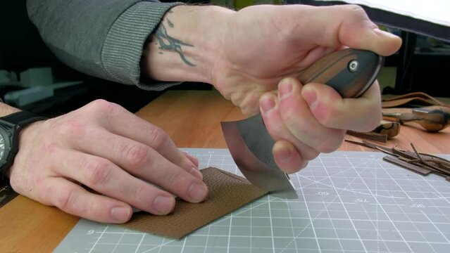 Close up hands tanner cuts special halberd cutting knife leather piece in workshop. Craft production.