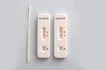 Two covid antigen rapid test kits and a nasal swab with positive results on white background, covid-19 lab testing concept