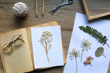 Old book, papers, various pressed flowers, eyeglasses, scissors, pencils and rope on wooden desk....