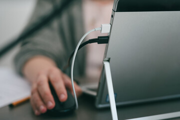 Close up of gray laptop being charge with usb charger plugged in while unrecognizable person working on it
